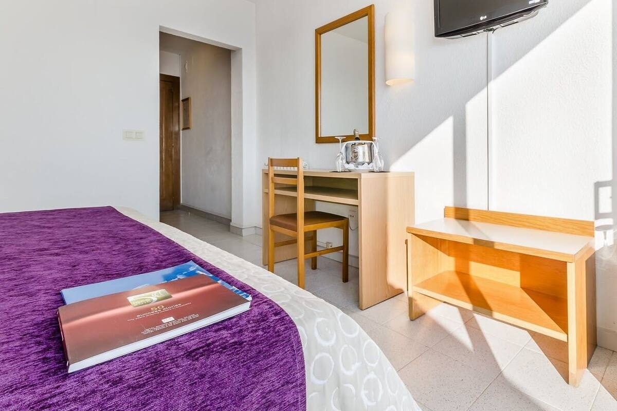 A hotel room with a bed, a desk, a chair, a TV, and a mirror.