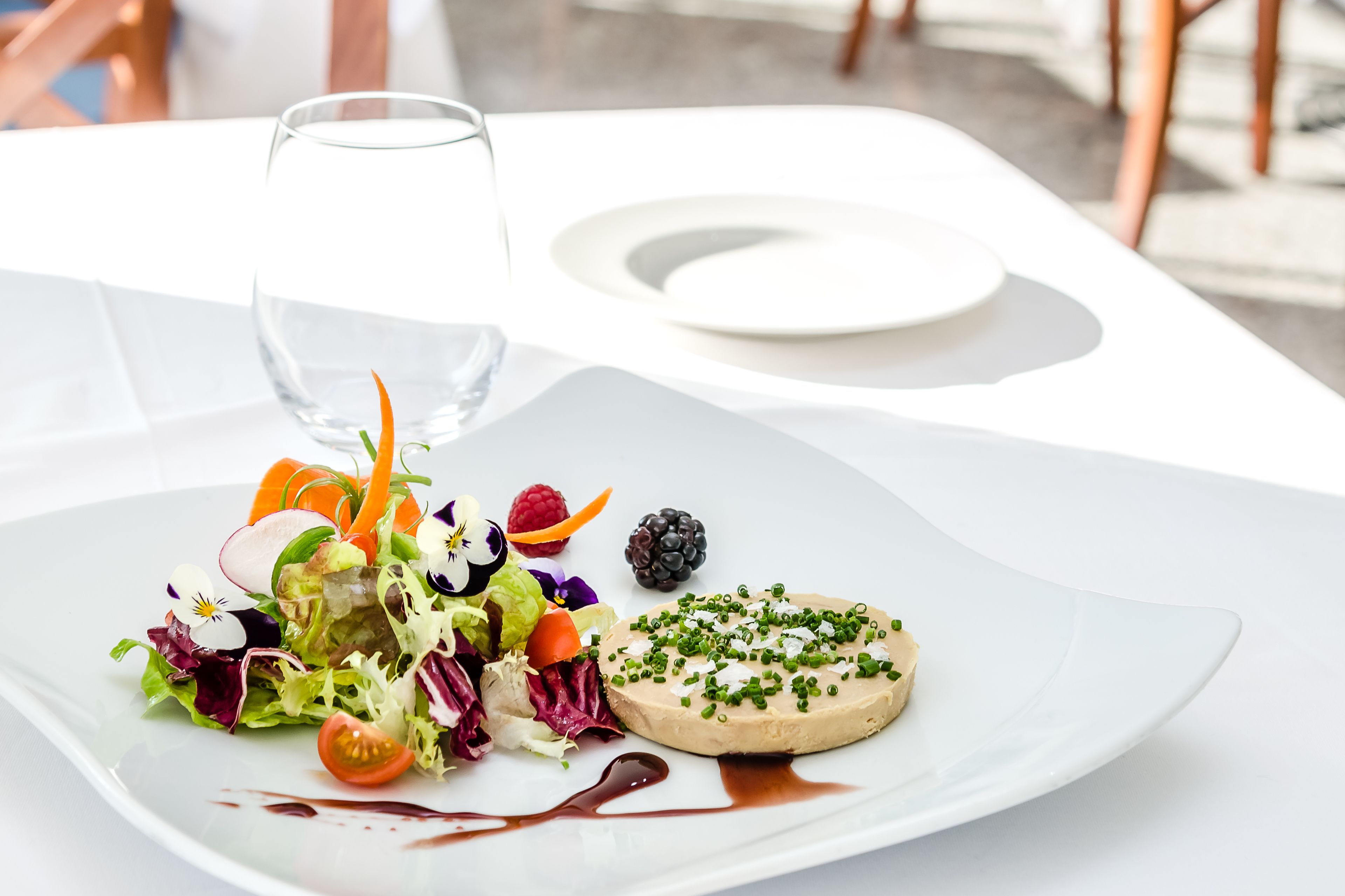 A white table with a plate of food, a glass of water, and a white plate.