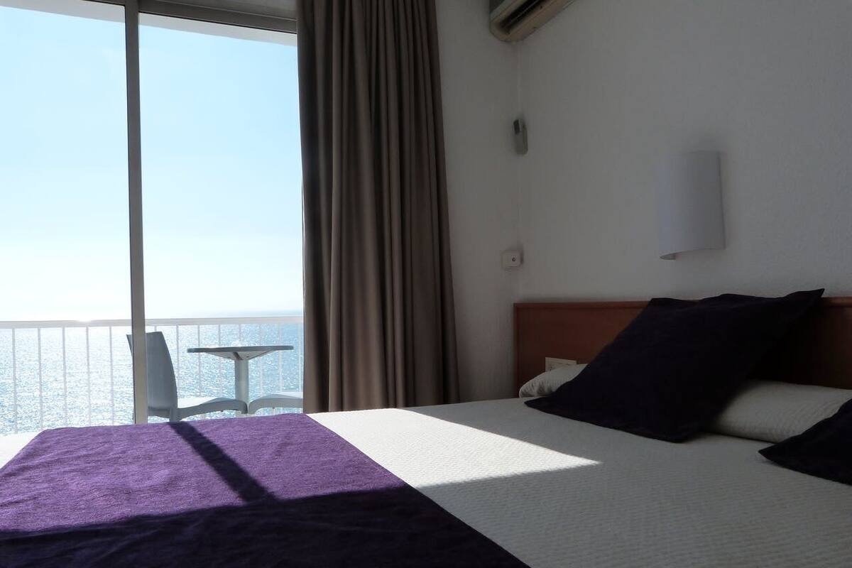 A hotel room with a bed, a chair, and a view of the sea.