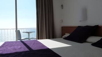 A hotel room with a bed, a chair, and a view of the sea.
