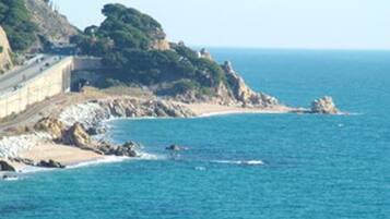 A coastal road with a guardrail, rocky shoreline, and a clear view of the sea.