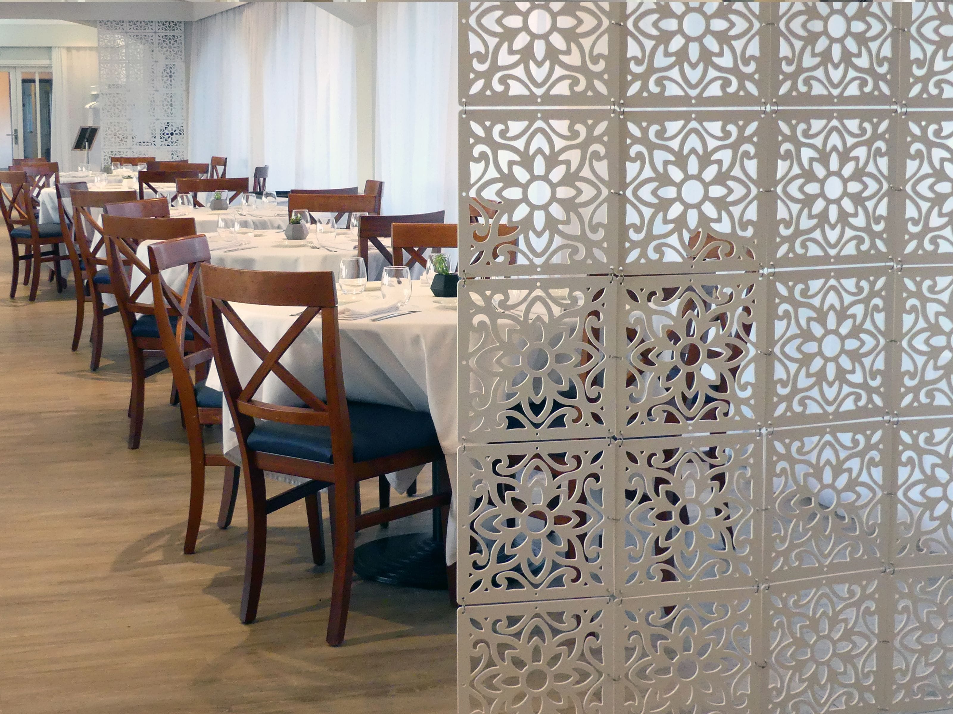 A dining area with wooden chairs and tables, a decorative white partition, and a piano in the background.
