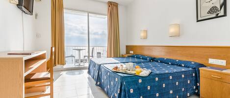 Habitación de hotel con cama, escritorio, silla, televisor y balcón con vistas.