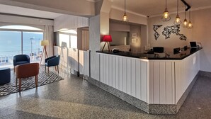 A modern hotel lobby with a reception desk, seating area, and large windows overlooking the sea. - Hotel Gran Sol (Sant Pol De Mar)