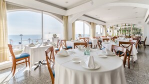 A restaurant with round tables, chairs, and a view of the sea. - Hotel Gran Sol (Sant Pol De Mar)