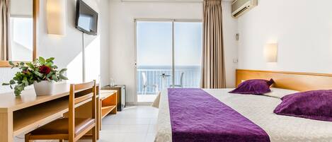 Habitación de hotel con cama, escritorio, silla, televisor y balcón con vistas.