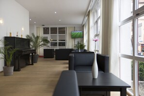 Un moderno vestíbulo de hotel con un piano, zona de estar y una pantalla de televisión.