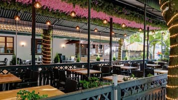Un espace de restauration en plein air, avec des tables et des chaises, entouré de verdure et de fleurs roses.