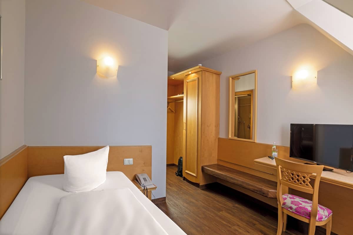 A hotel room with a bed, a desk with a chair, a television, and a wardrobe.