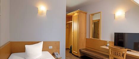 Una habitación de hotel con cama, escritorio, silla, televisor y armario.