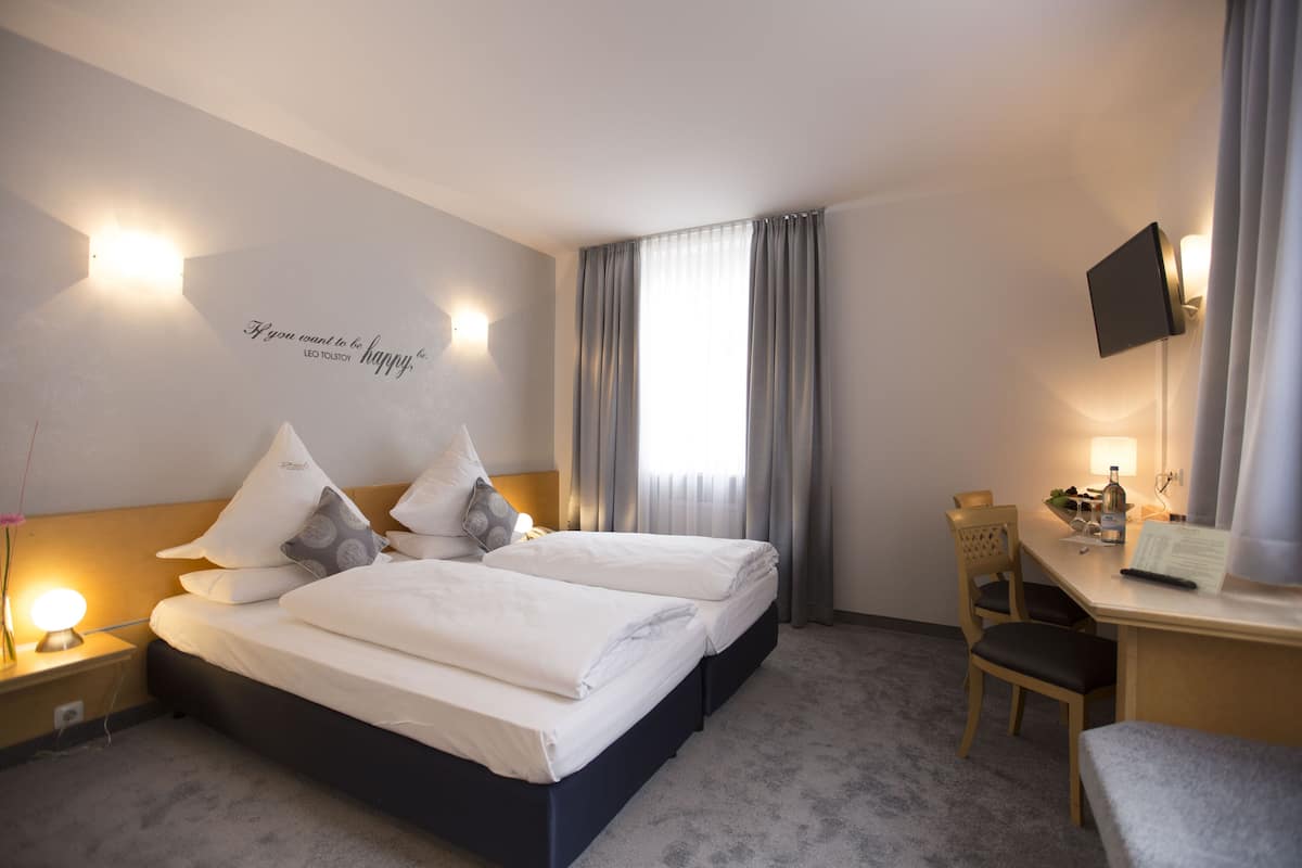 A hotel room with two beds, a desk, a chair, a TV, and a wall with a motivational quote.