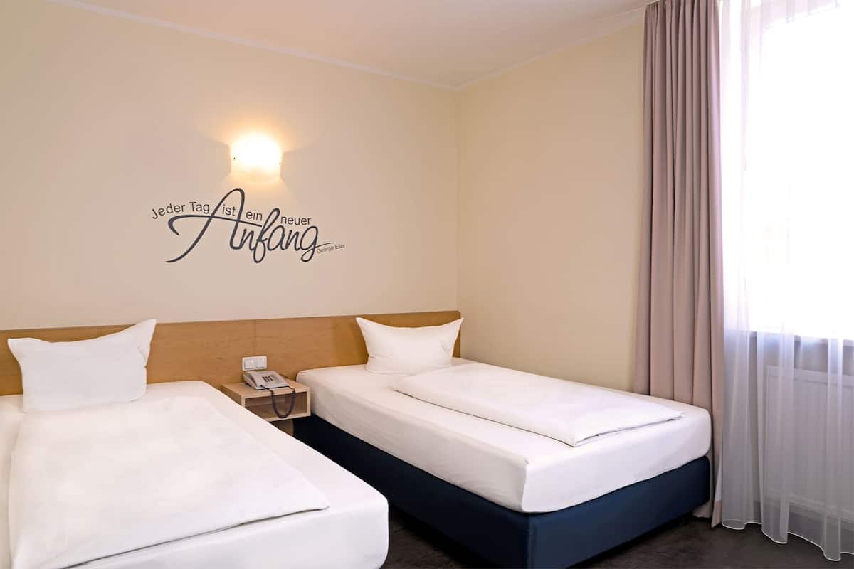 A hotel room with two beds, a wall-mounted light, and a sign with text.