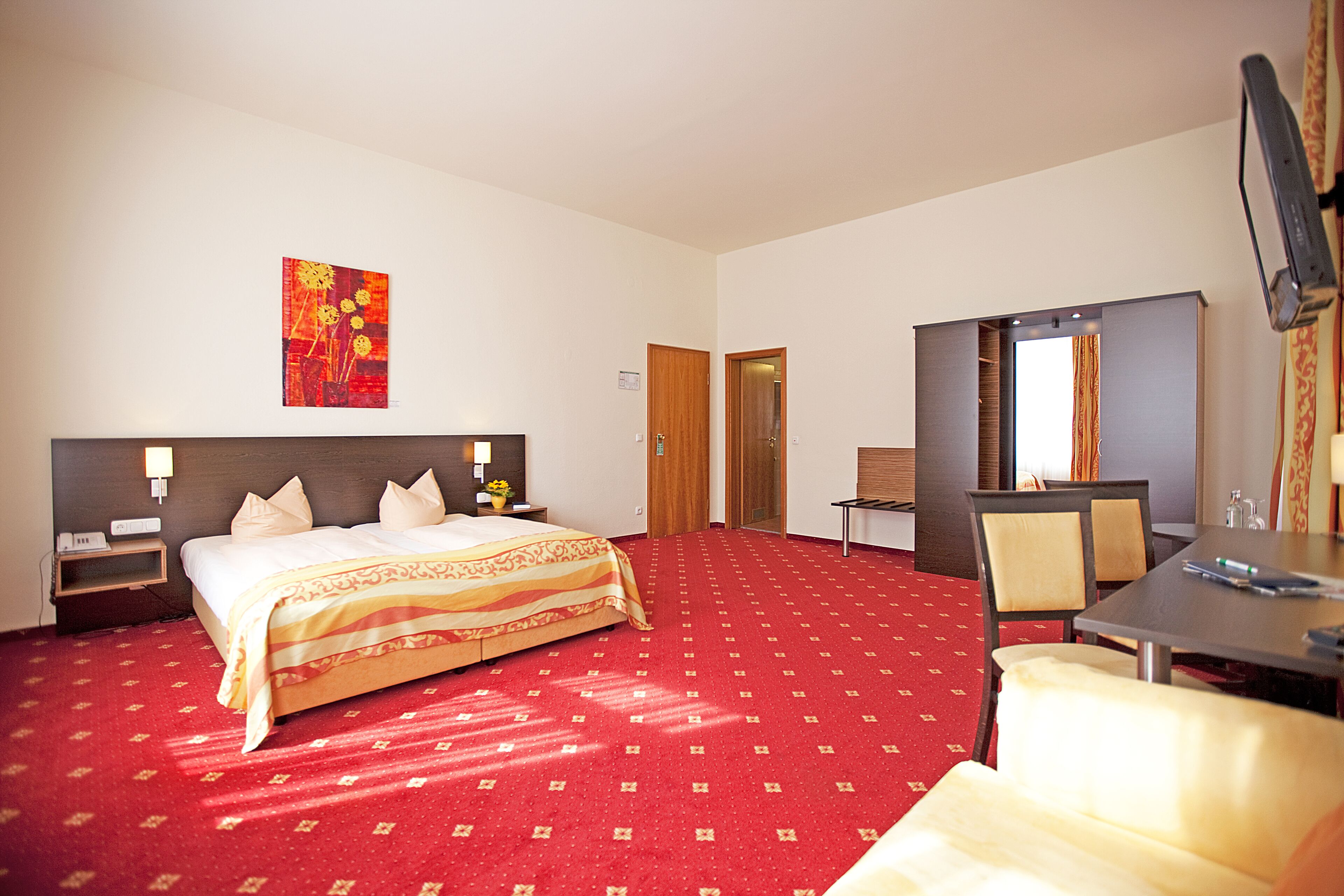 Une chambre d’hôtel avec un lit, des tables de chevet, un bureau, une chaise, une télévision et un tableau au mur.