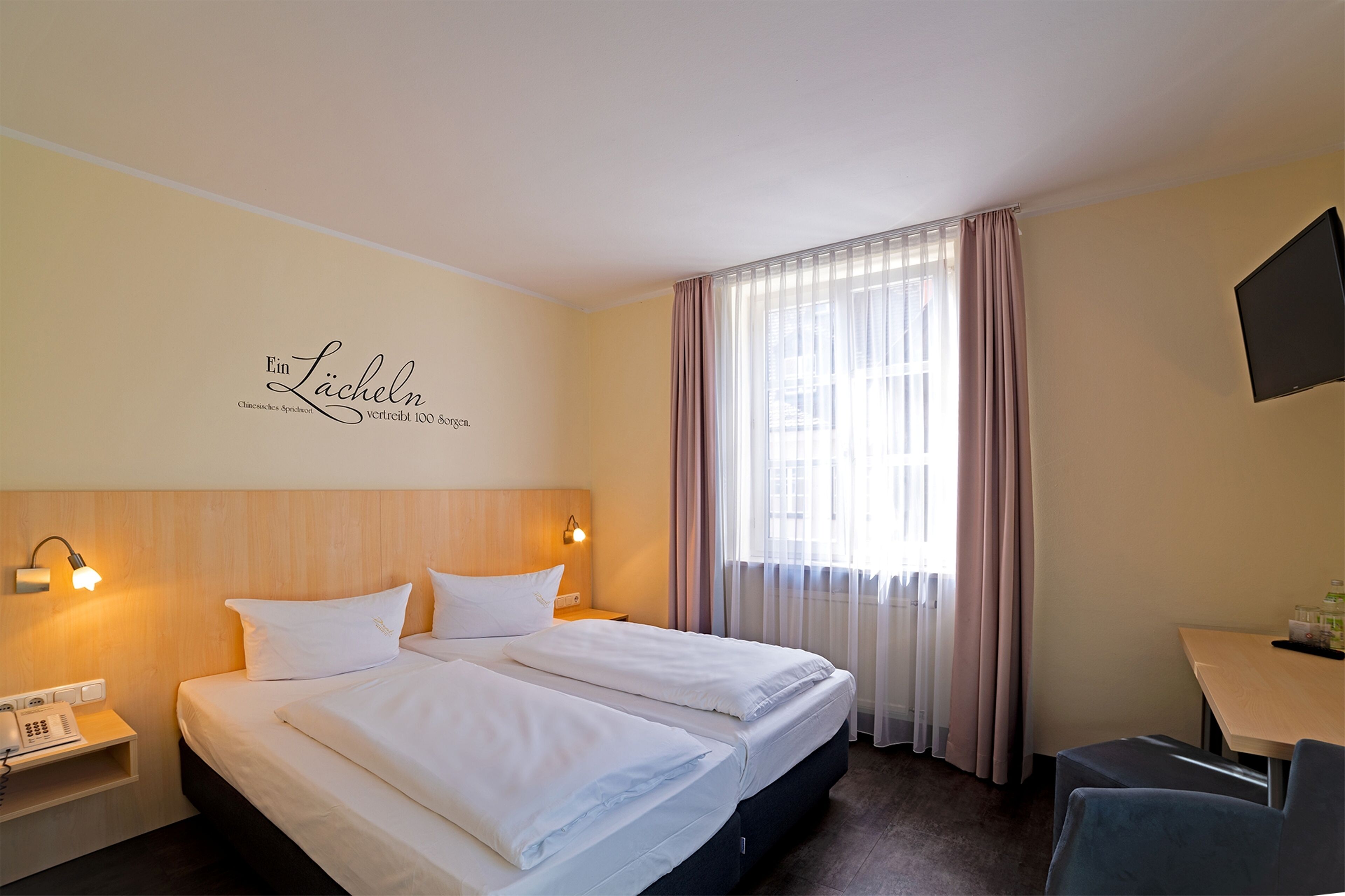 A hotel room with a bed, bedside lamps, a desk, and a television.