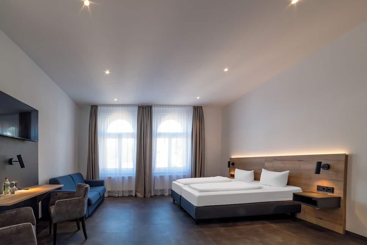 A modern hotel room with a large bed, a desk, a chair, and a TV mounted on the wall.