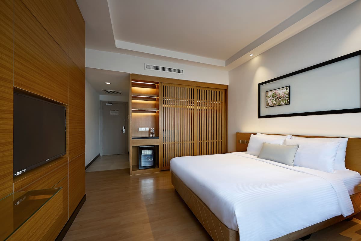 A hotel room with a large bed, a flat-screen TV, wooden paneling, a small kitchenette, and a framed picture on the wall.