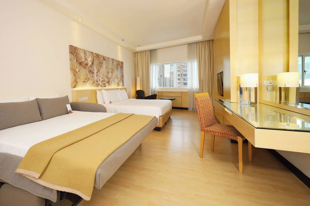 A hotel room with two beds, a desk, a chair, a large mirror, and a view of the city through the window.