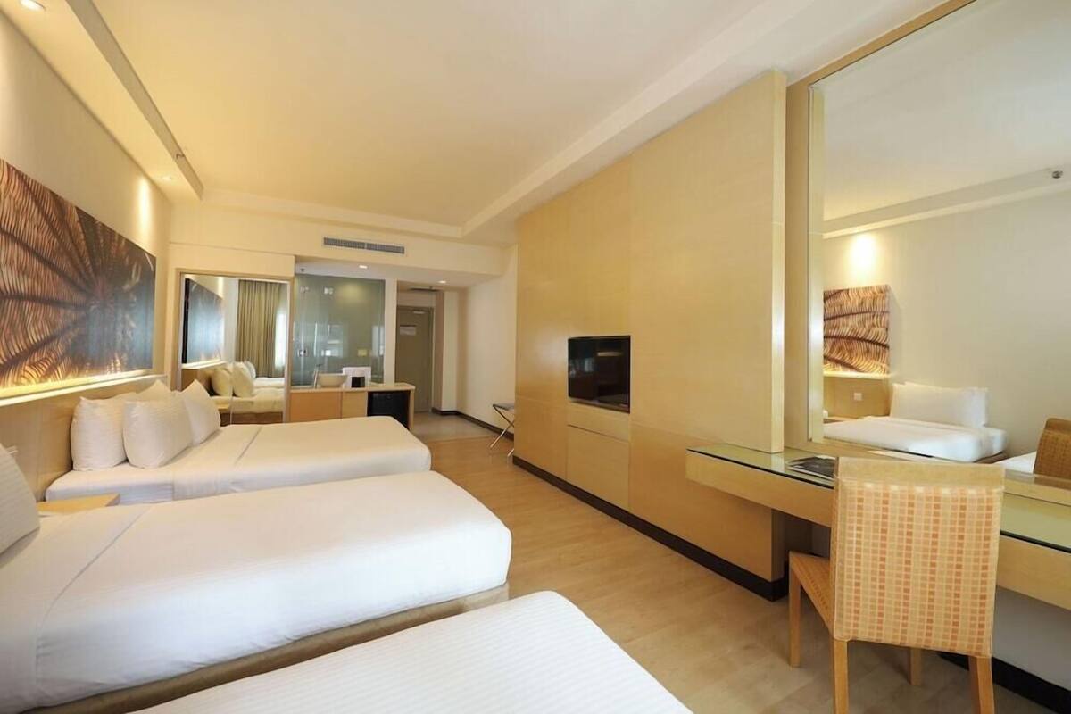 A hotel room with two beds, a desk, a chair, a TV, and a large mirror.