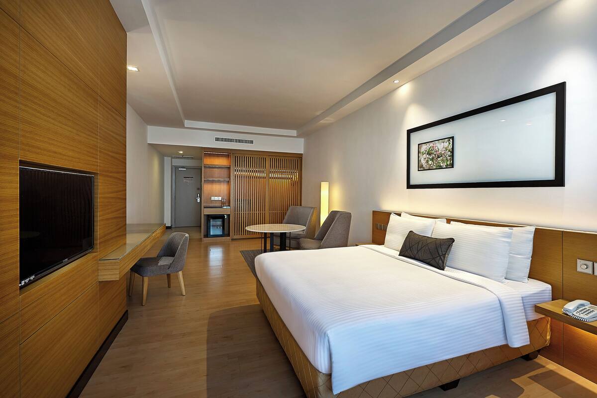 A modern hotel room with a large bed, a flat-screen TV, a desk, and a seating area with chairs.