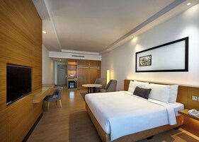A modern hotel room with a large bed, a flat-screen TV, a desk, and a seating area with chairs.