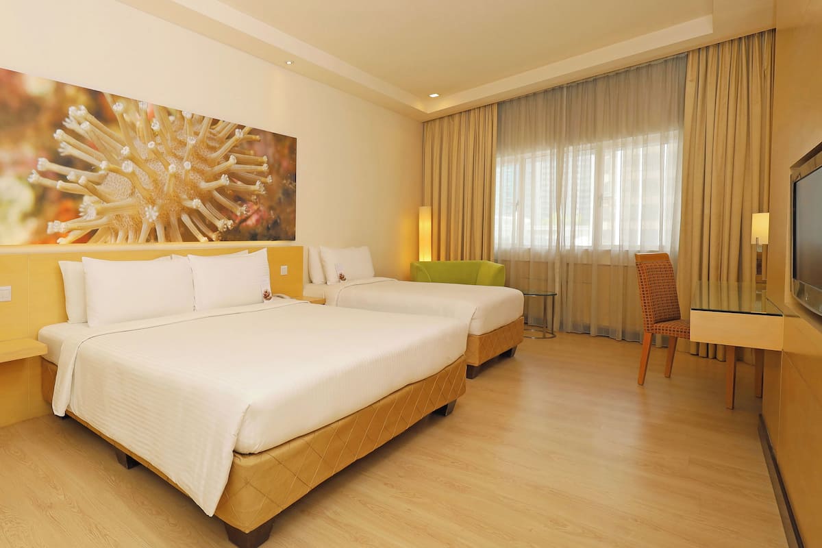 A hotel room with a large bed, a smaller bed, a desk, a chair, and a television.