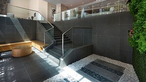 Un interno moderno con una scala, ringhiere in vetro e un muro in pietra con piante.