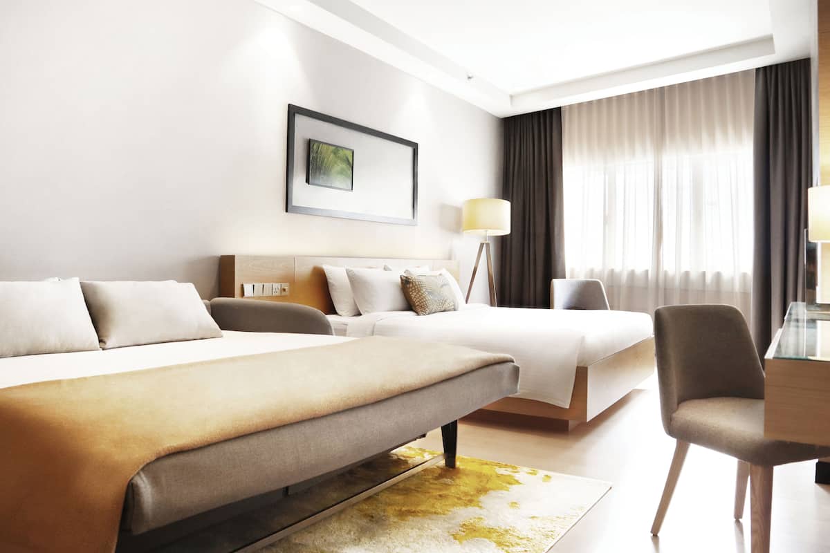 A hotel room with a large bed, a smaller bed, a desk with a chair, a floor lamp, and a painting on the wall.