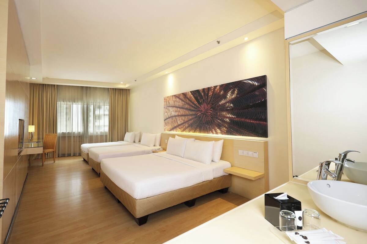 A hotel room with two beds, a desk, a chair, a large mirror, and a bathroom with a sink and mirror.