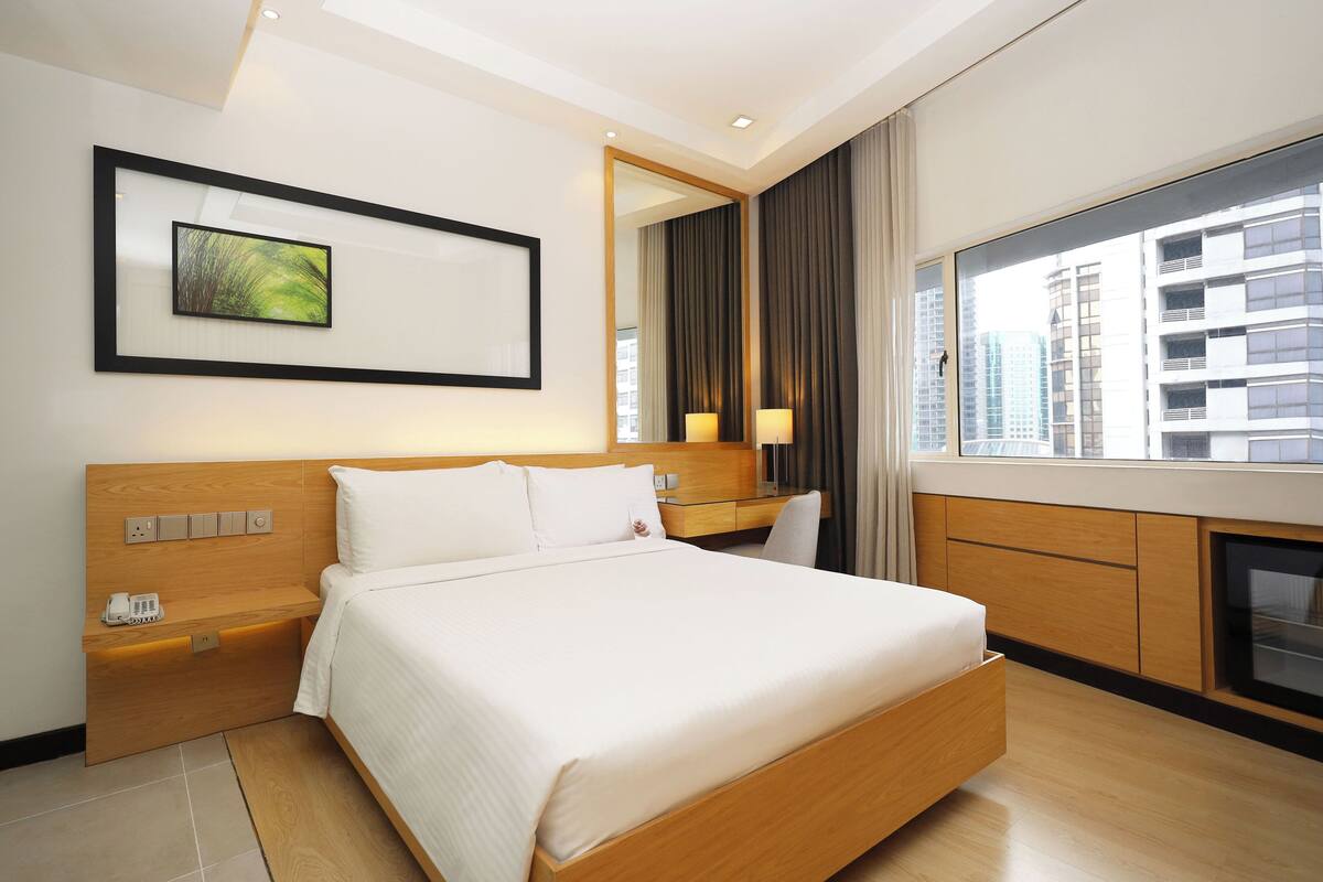 A modern hotel room with a large bed, bedside tables, a desk, and a view of the city.