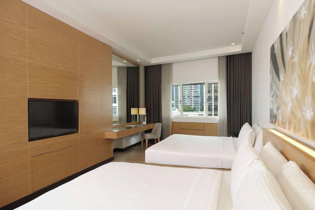 A hotel room with two beds, a desk, a TV, a chair, and a large window with curtains.