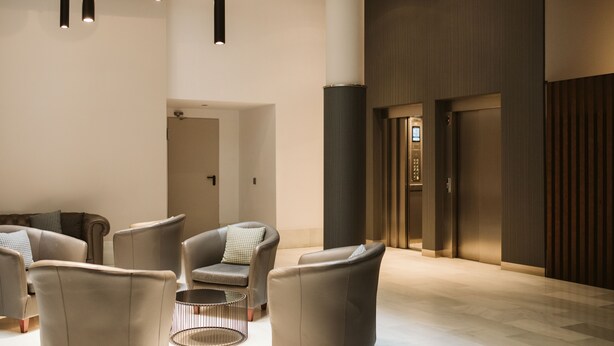 Un hall d’entrée moderne avec des fauteuils en cuir, une table basse ronde et une grande colonne cylindrique.