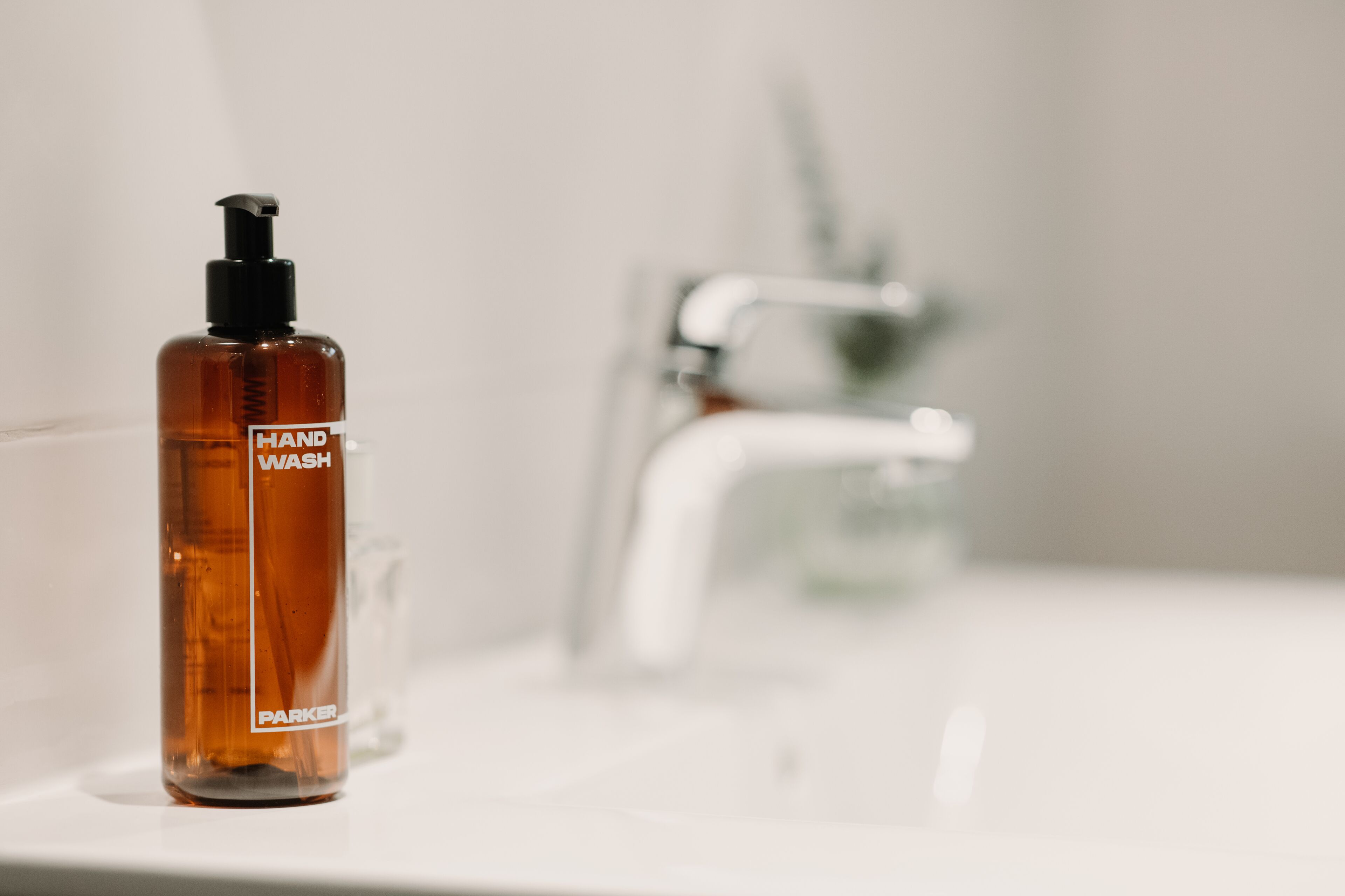 Eine Handseifenflasche mit dem Aufdruck 'HAND WASH' auf einem Badezimmerwaschbecken.