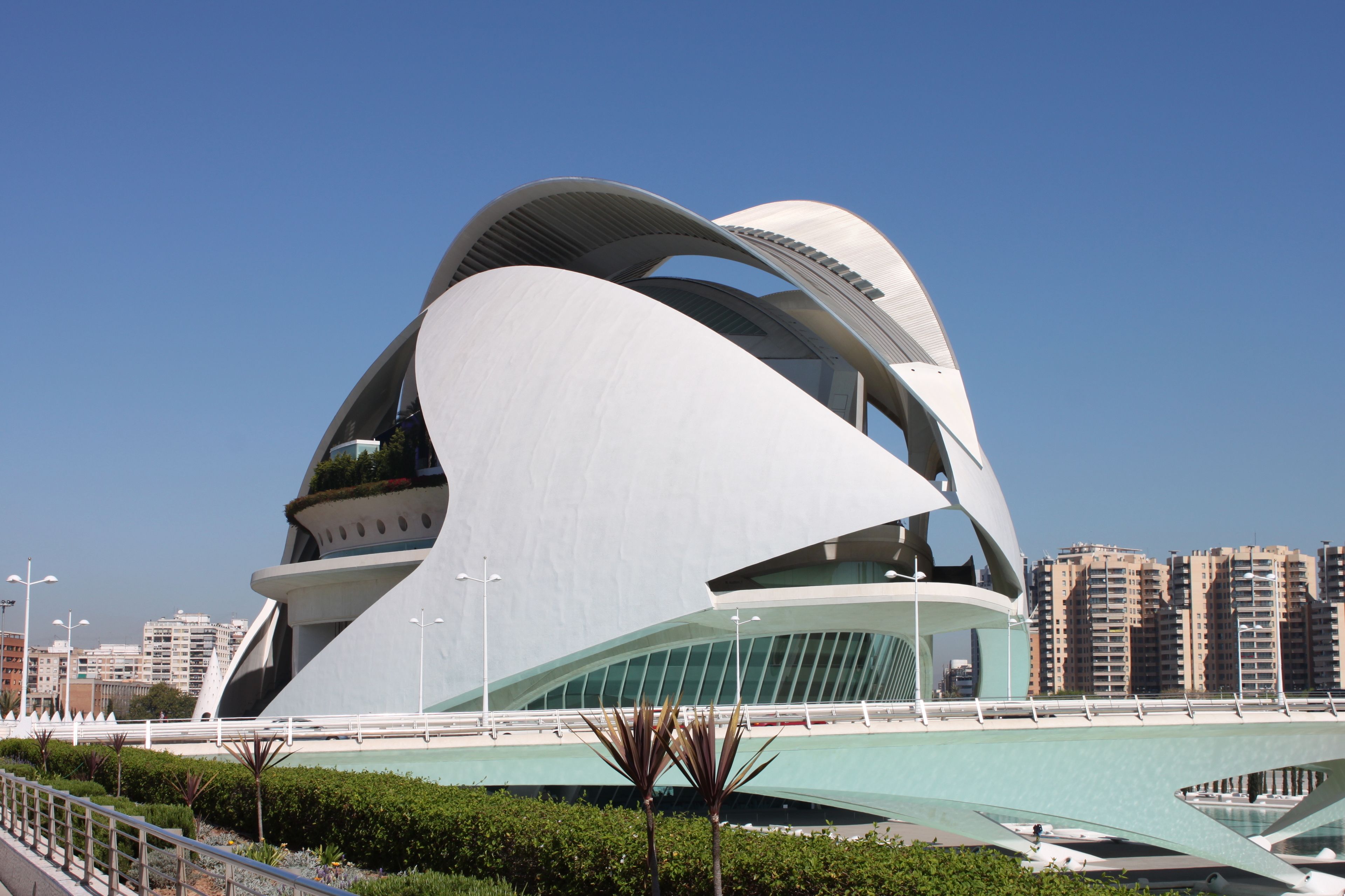Un edificio de arquitectura moderna con un diseño curvo único, rodeado de vegetación y un cielo despejado.