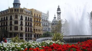 Un edificio histórico con arquitectura ornamentada, una fuente y coloridos jardines de flores.