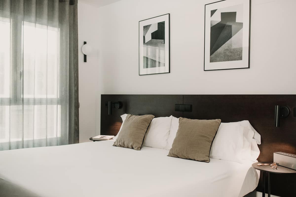 Ein modernes Hotelzimmer mit einem großen Bett, zwei Kissen, einem Nachttisch und zwei gerahmten Bildern an der Wand.
