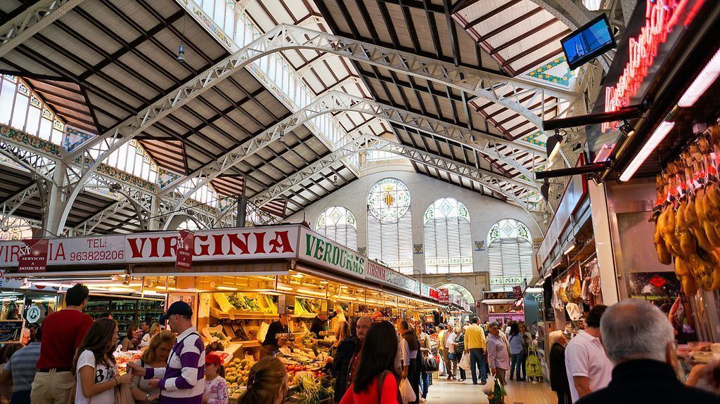 An indoor market with a high ceiling and arches, featuring a fruit and vegetable stall named "Virginia Verduras."