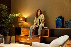 A person sitting on a wooden bench in a room with a lamp, blue vases, and a potted plant. - Parker The Urban Flats (Valencia)