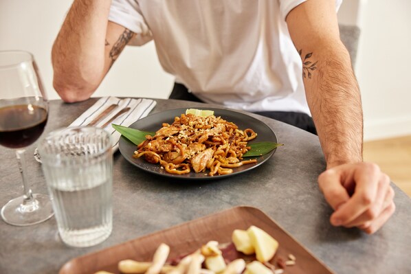A person sitting at a table with a plate of noodles, a glass of red wine, and a water glass. - Parker The Urban Flats (Valencia)