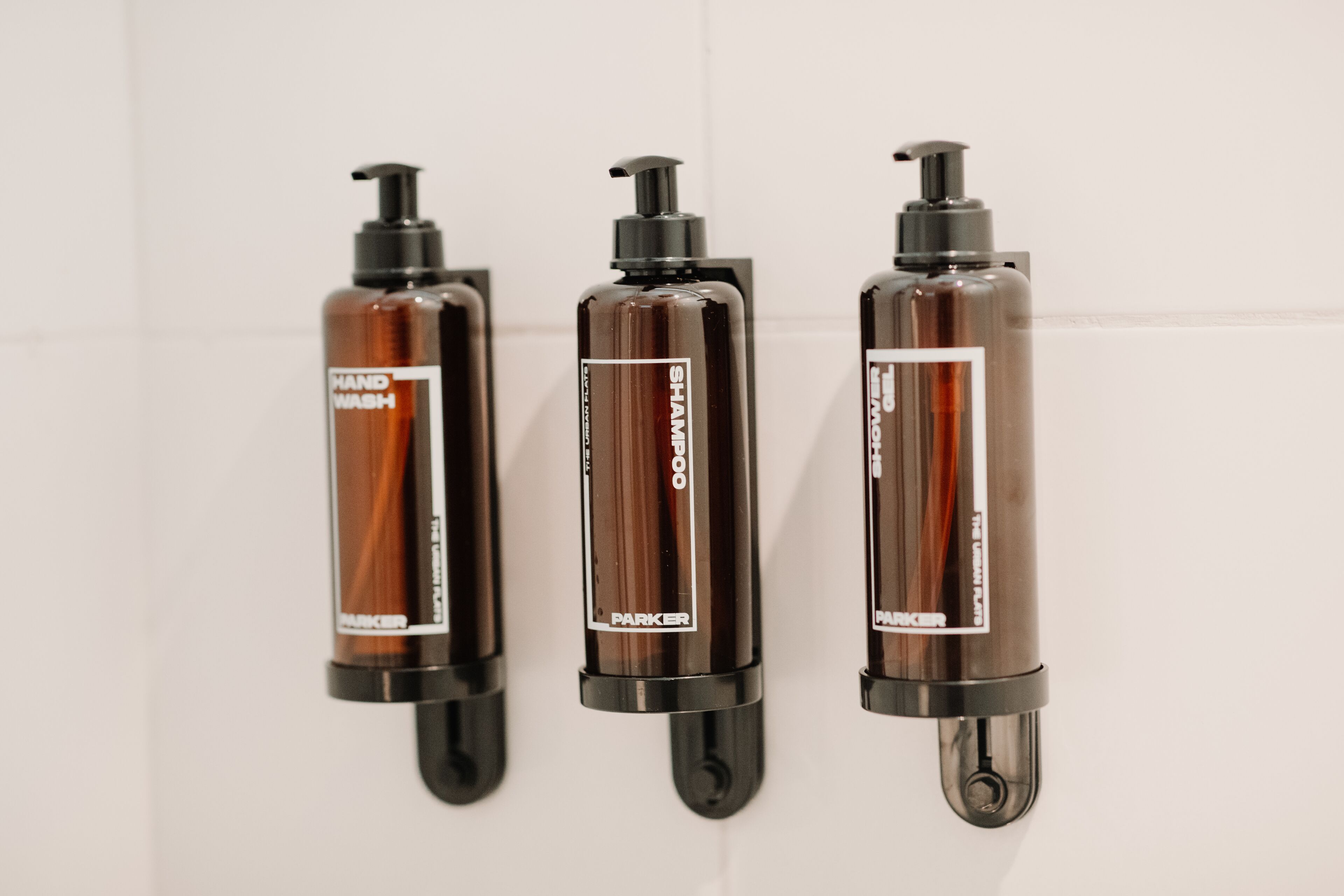 Three hand wash bottles mounted on a wall.