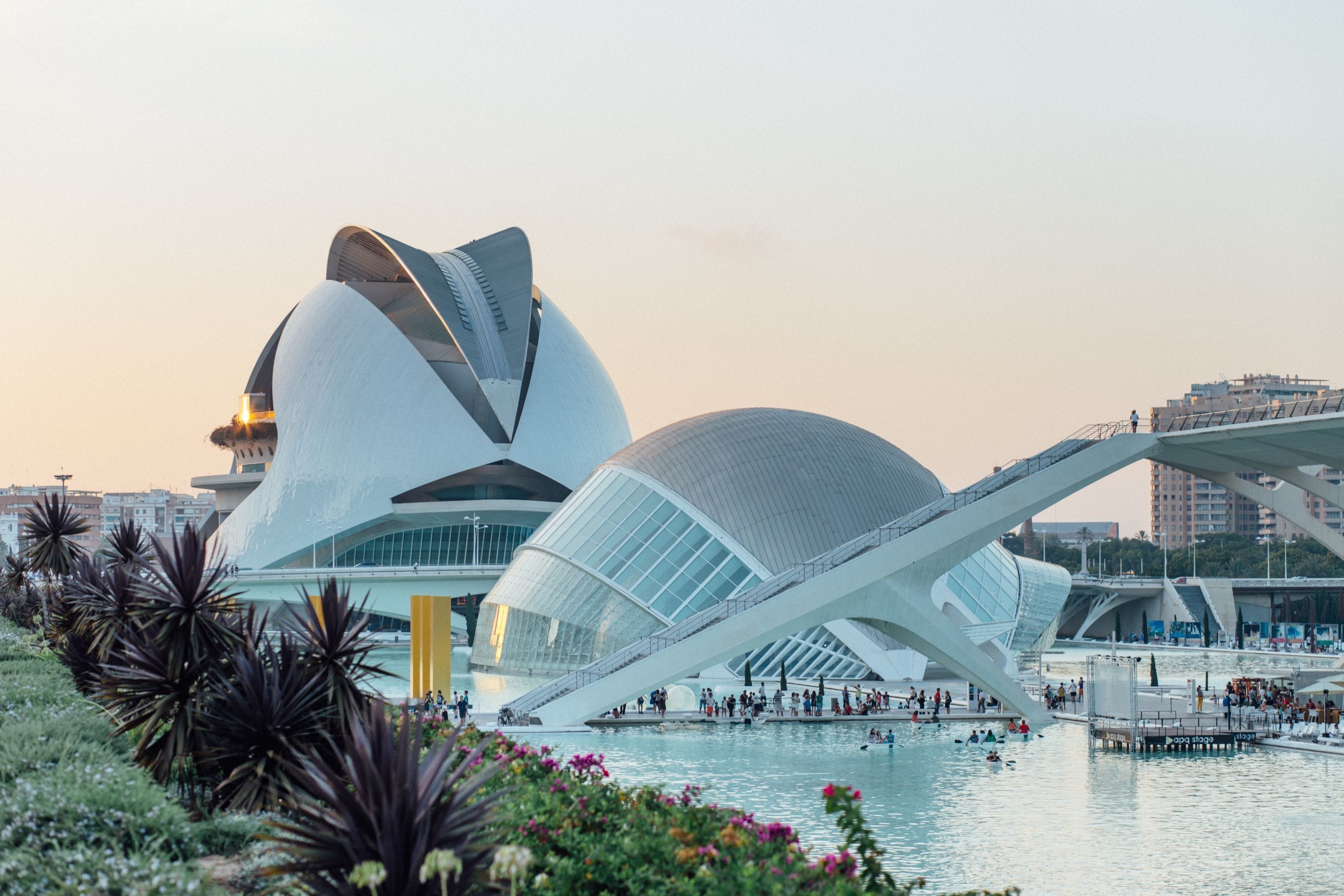 A modern architectural structure with a unique curved design, a large open plaza, and a body of water in the foreground.