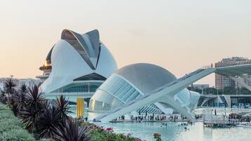 A modern architectural structure with a unique curved design, a large open plaza, and a body of water in the foreground.