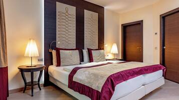 A hotel room with a large bed, two bedside tables with lamps, a headboard with decorative panels, and a door.