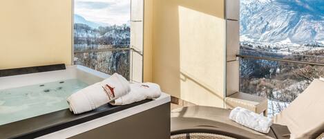 Un área de spa con una bañera y una silla de descanso, ambos con toallas, con vistas a un paisaje montañoso nevado.