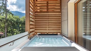 Un bain à remous doté d’un plafond en bois et de parois en verre, offrant une vue sur un paysage montagneux.