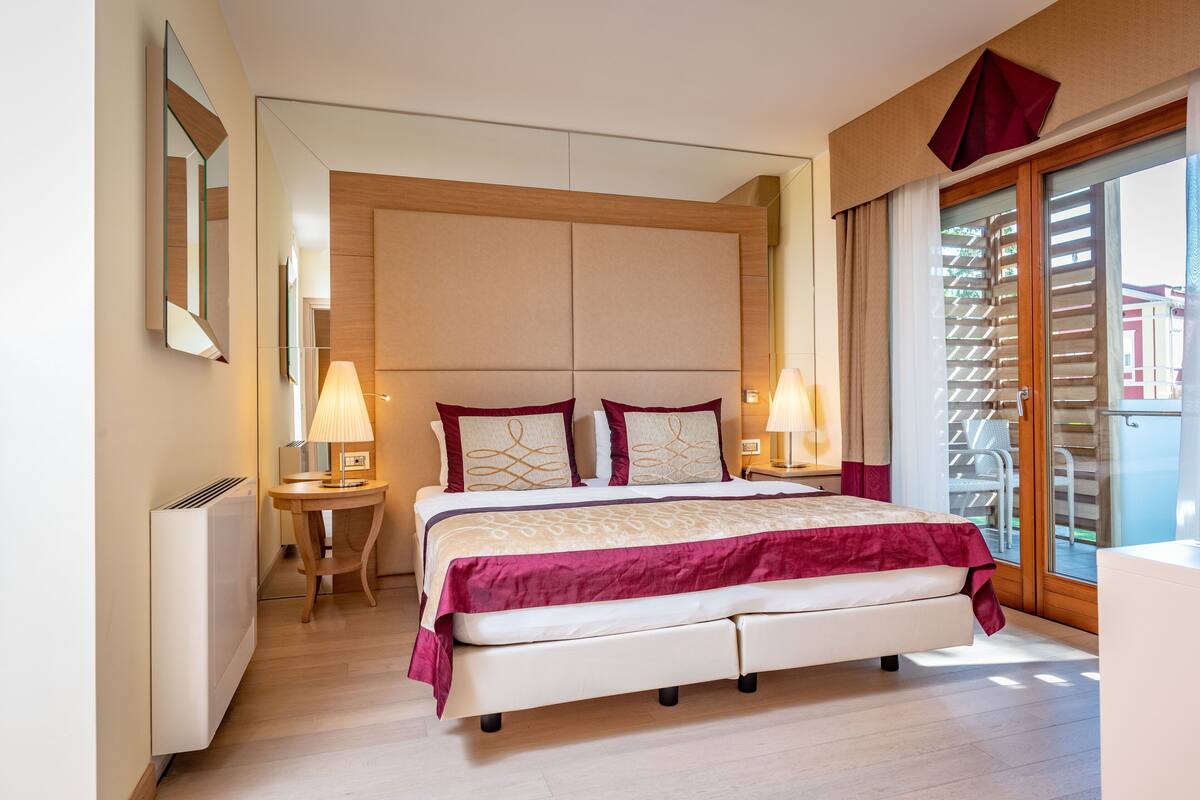 Ein modernes Schlafzimmer mit einem großen Bett, zwei Nachttischen mit Lampen, einem Holz-Kopfende und einer Glastür zum Balkon.