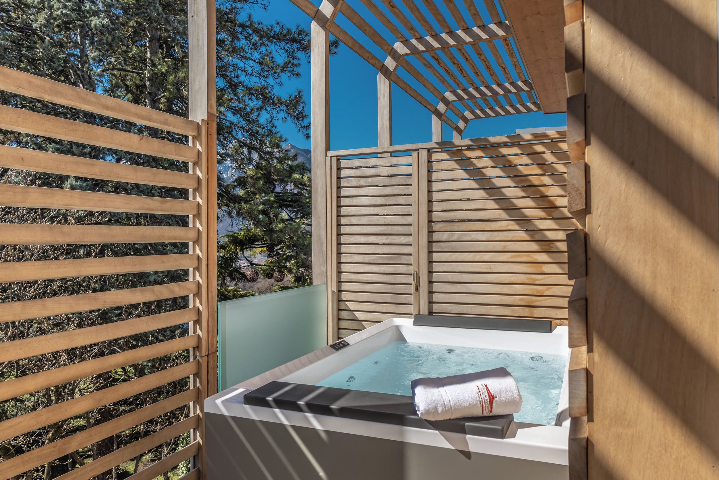 Un espacio exterior de spa con madera, que incluye un jacuzzi, listones de madera y vistas a árboles.