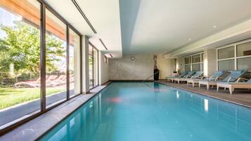 Ein modernes Hallenbad mit großen Fenstern, Liegestühlen und einer Uhr an der Wand.