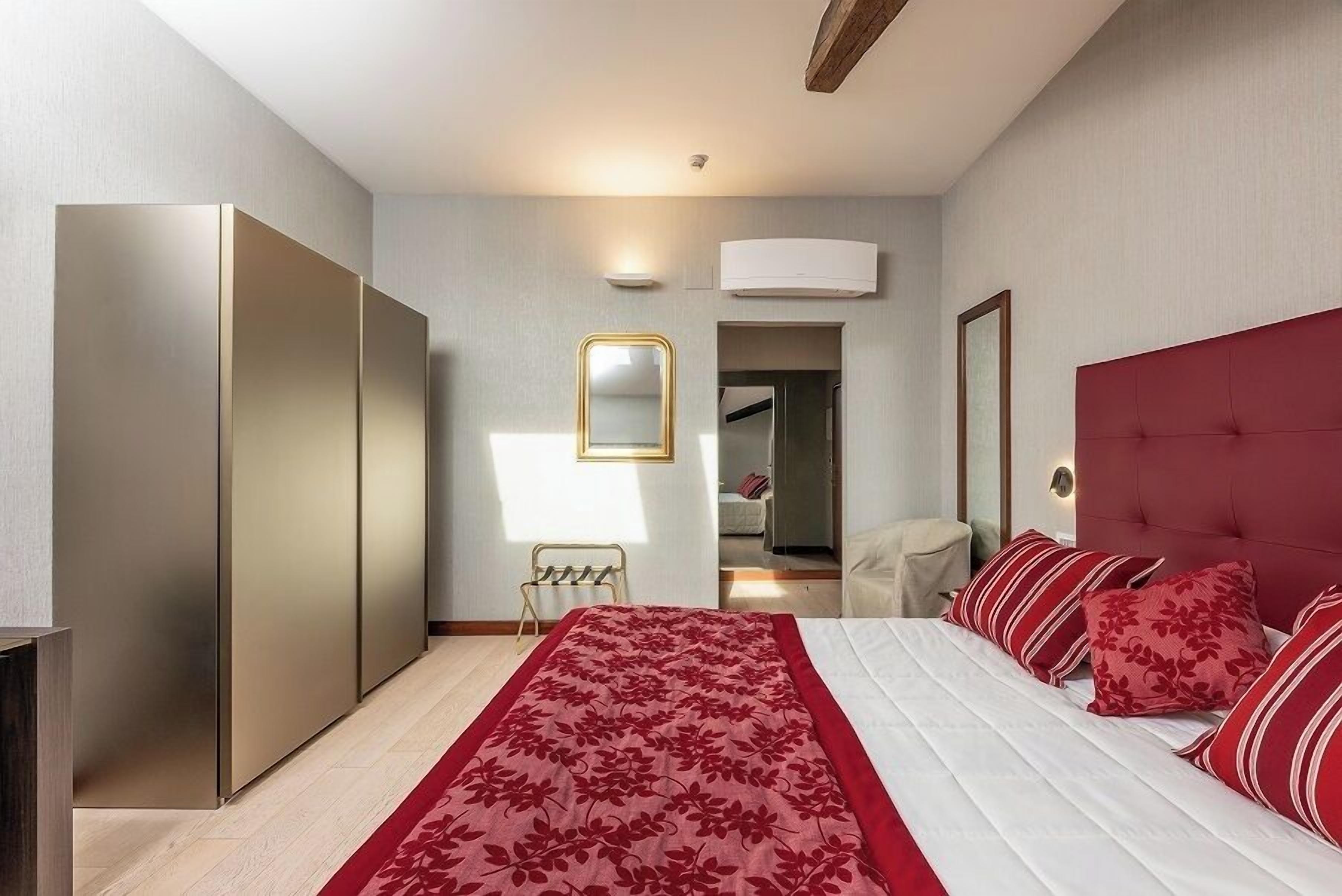 A modern bedroom with a large bed, a wardrobe, a mirror, and a red upholstered headboard.
