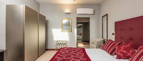 A modern bedroom with a large bed, a wardrobe, a mirror, and a red upholstered headboard.