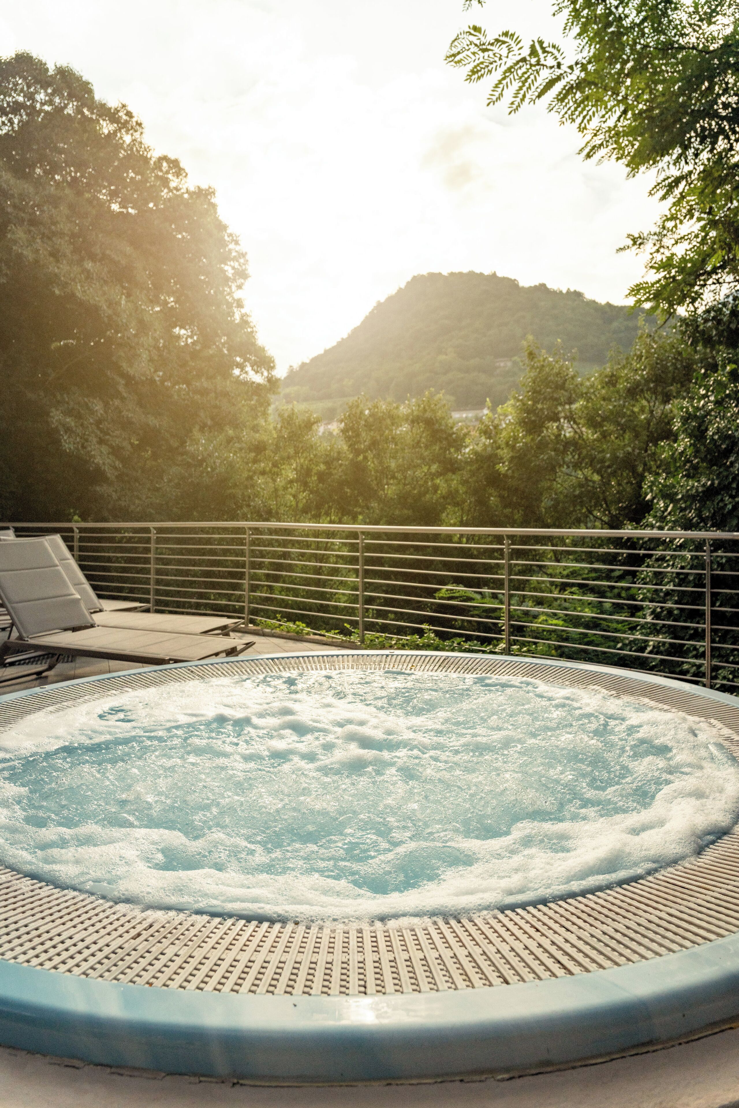 Un jacuzzi con baranda metálica y vista a una colina boscosa al fondo.